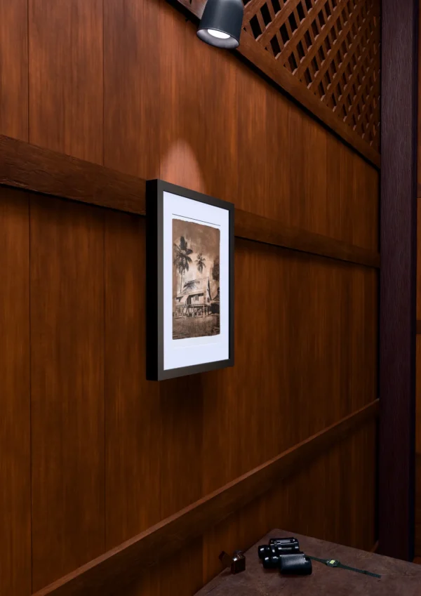 Vintage in Sepia, gel plate monotype by Daniel Arendzen, framed on a wooden wall under a spotlight, seen from the side, with binoculars, a watch and a lighter on a table below. The room is a Blender render of the interior of the same traditional Malaysian house shown in the print.